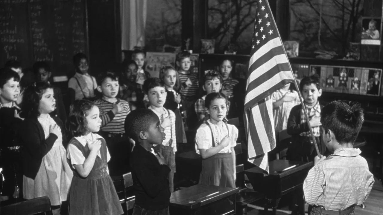 A mid 20th century American classroom scene with students standing beside their desks facing a flag, archival news photography style