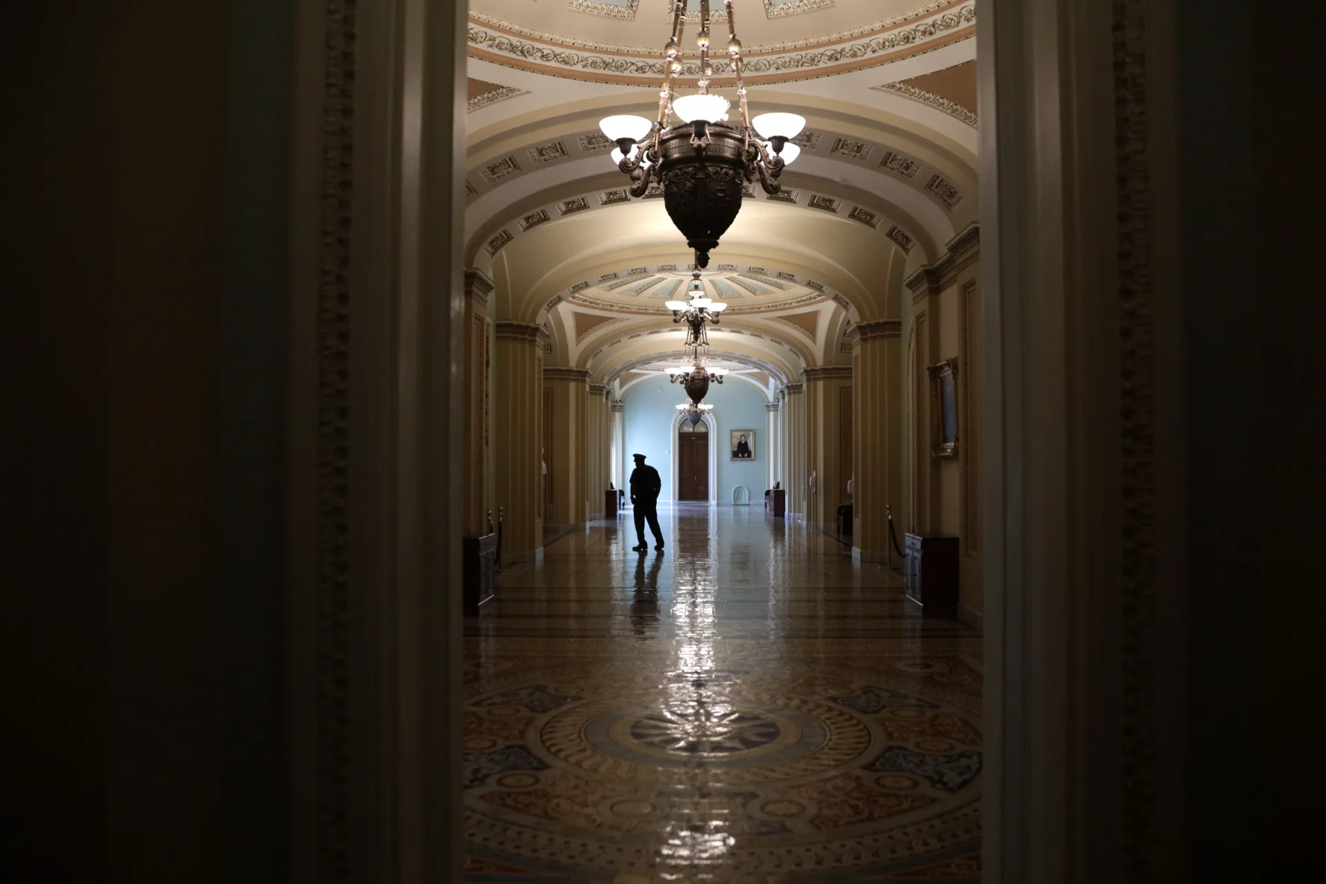A news-style photograph of a quiet corridor on the Senate side of the United States Capitol with aides walking past marble columns