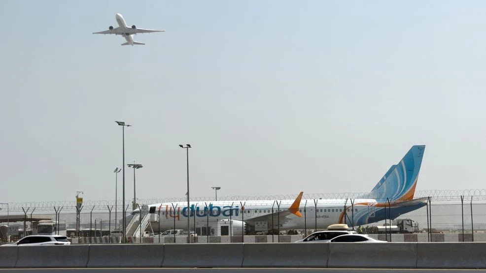 A passenger jet on the tarmac at Prince Sultan bin Abdulaziz Airport (Tabuk Airport) in Saudi Arabia, with airport buildings in the background