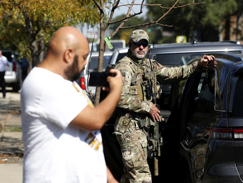 A person holding up a smartphone near a U.S. Border Patrol agent during an immigration enforcement operation in Chicago in October 2025, news photography style