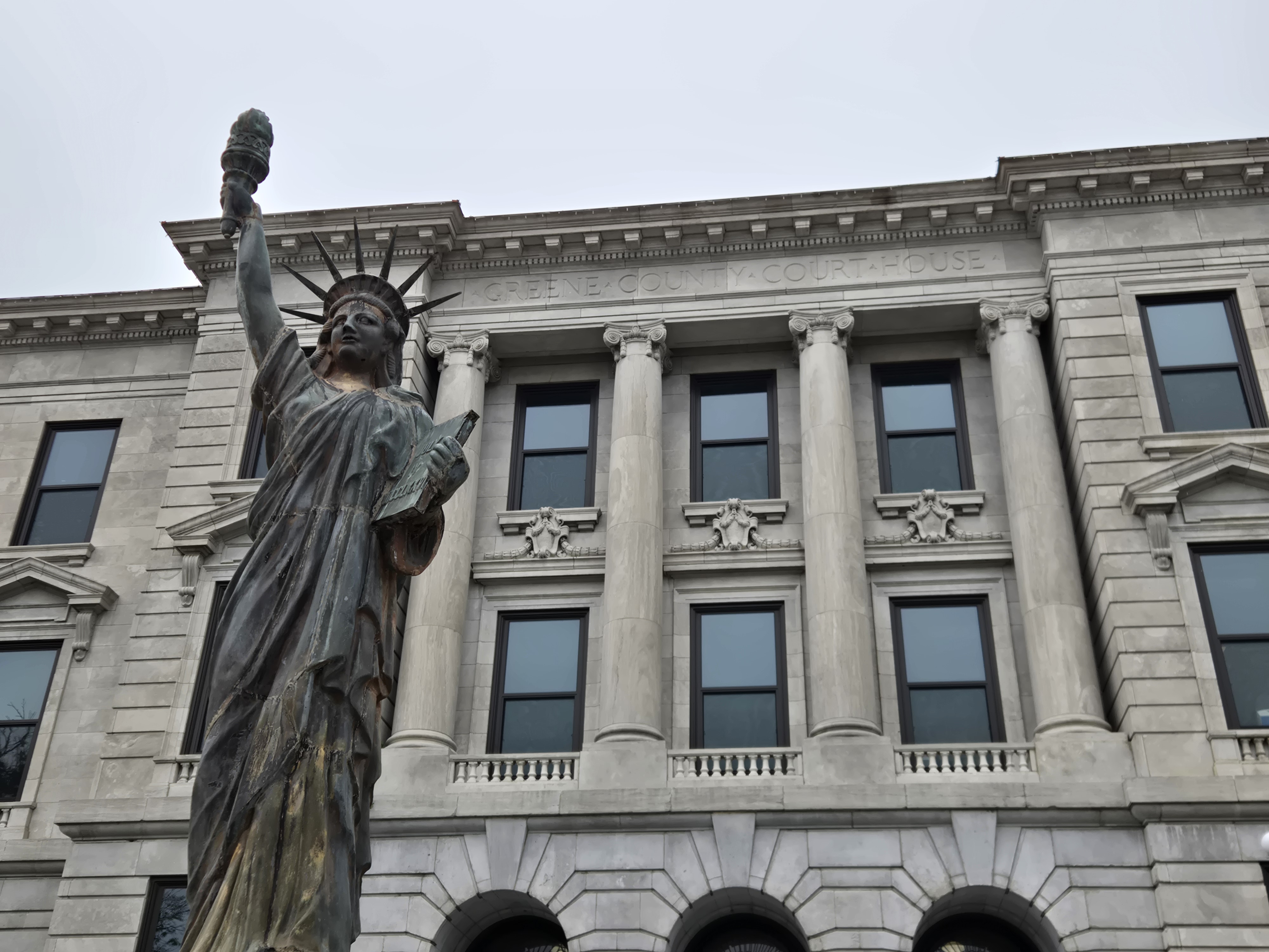 A person in business attire standing at a courthouse clerk window holding a stack of legal papers, documentary courtroom photography style