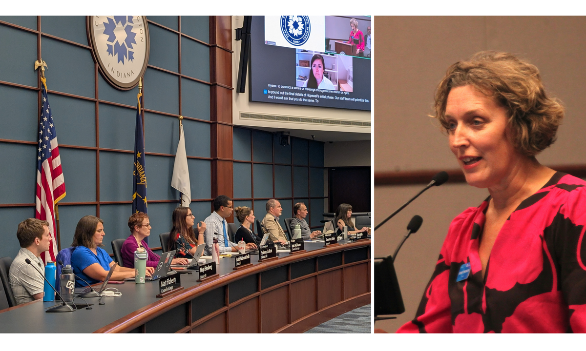 A person speaking at a press conference with several microphones in the foreground and a city hall building blurred behind, realistic news photography style