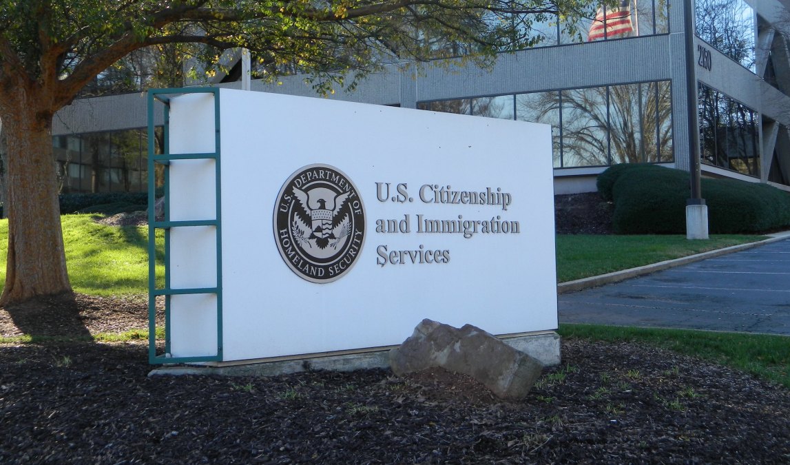 A photograph of an exterior sign at a USCIS field office, showing the agency name and entrance area