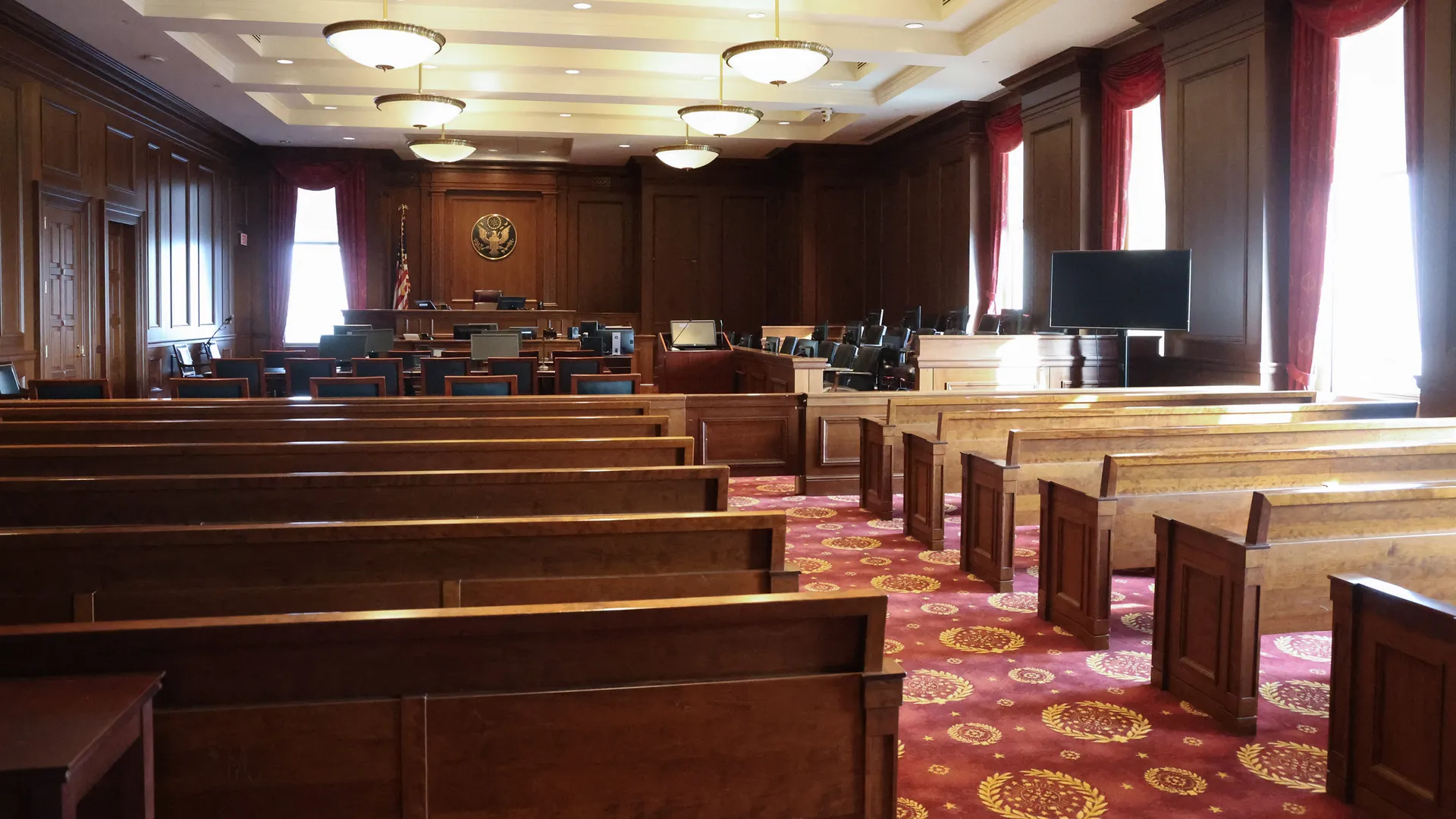 A photograph taken inside a federal courtroom showing the judge’s bench, the American flag, and empty counsel tables before proceedings begin