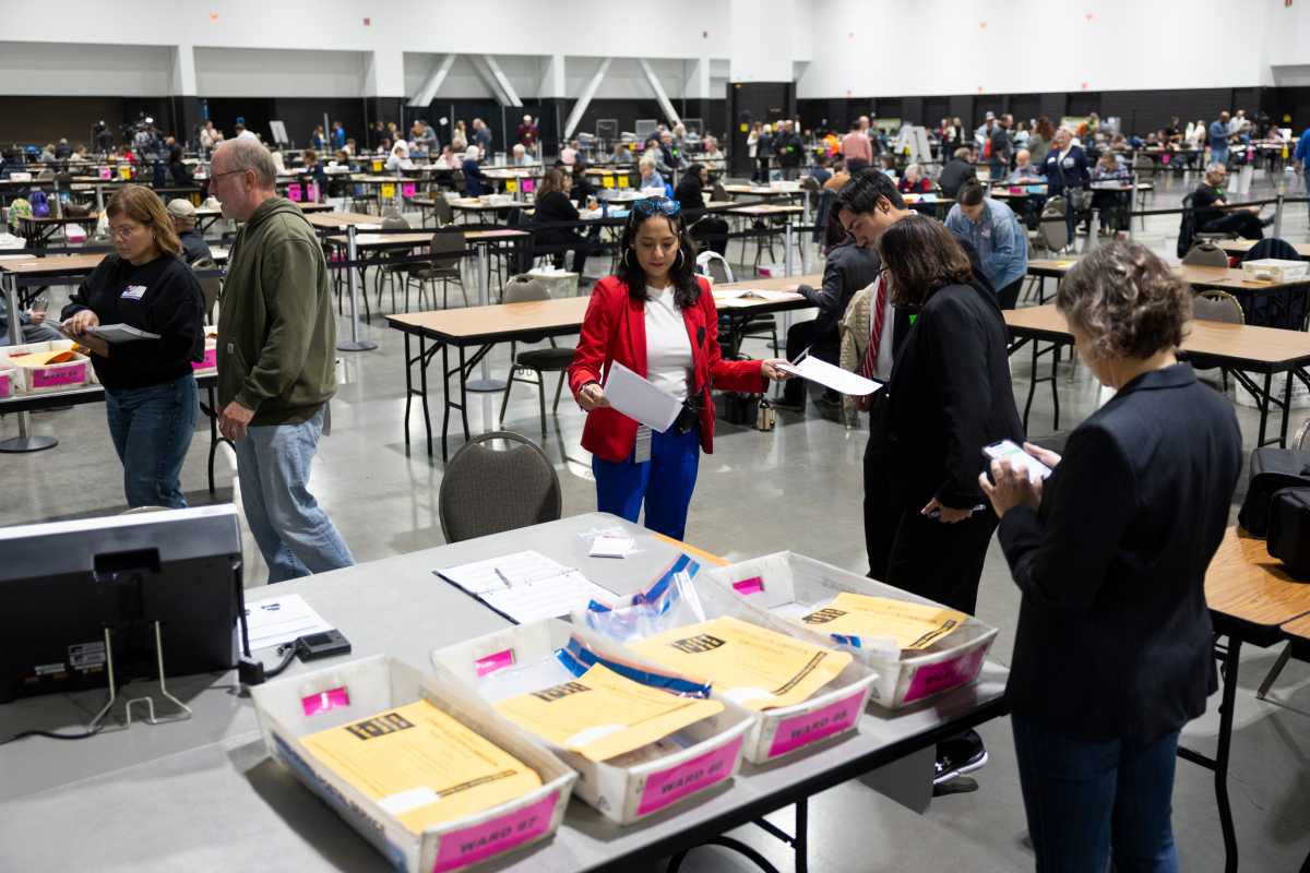 A poll worker checking a voter in at an Election Day table inside a Milwaukee, Wisconsin polling place, with voting booths visible in the background, documentary news photograph