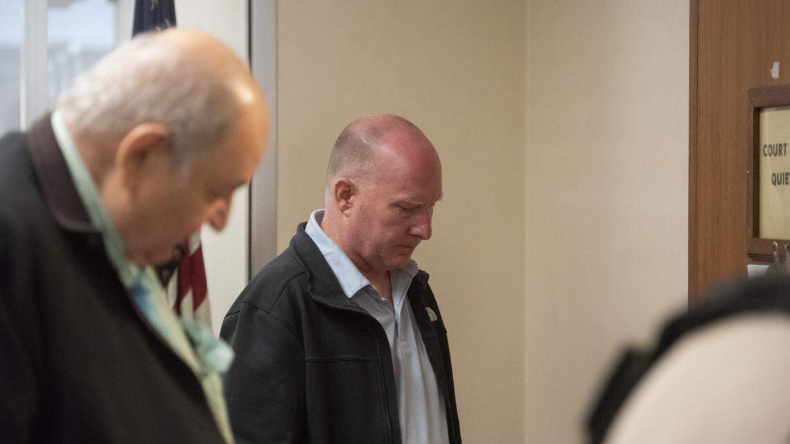 A process server in business attire handing a thick envelope to an adult outside a county courthouse entrance in daylight, news photography style