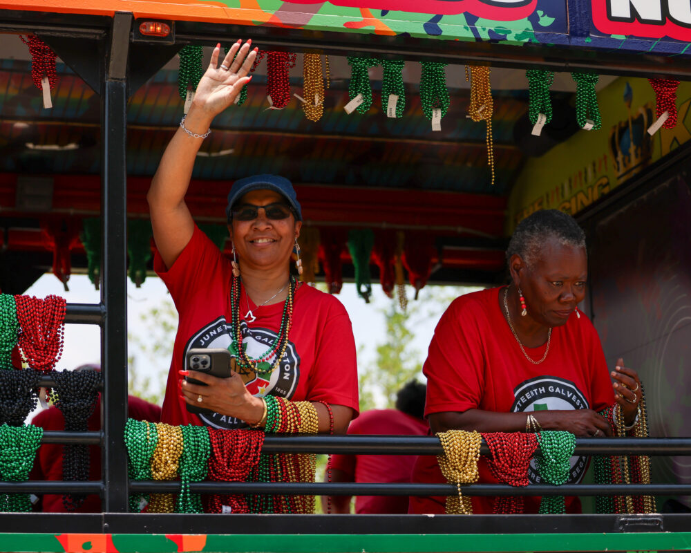 A public Juneteenth celebration in Galveston, Texas, with community members marching outdoors and carrying Juneteenth-themed flags in daylight