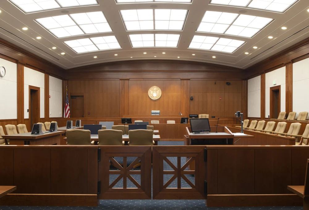 A quiet United States District Court courtroom with the judge’s bench, counsel tables, and gallery seating visible, news photography style