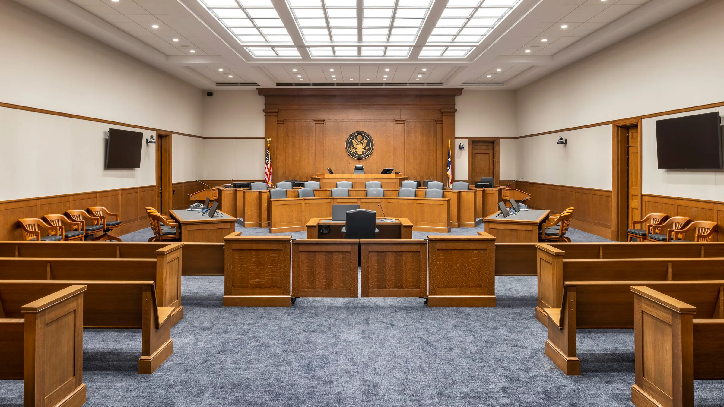 A quiet federal courtroom with an empty jury box, counsel tables, and the judge’s bench in view before proceedings begin, news photography style