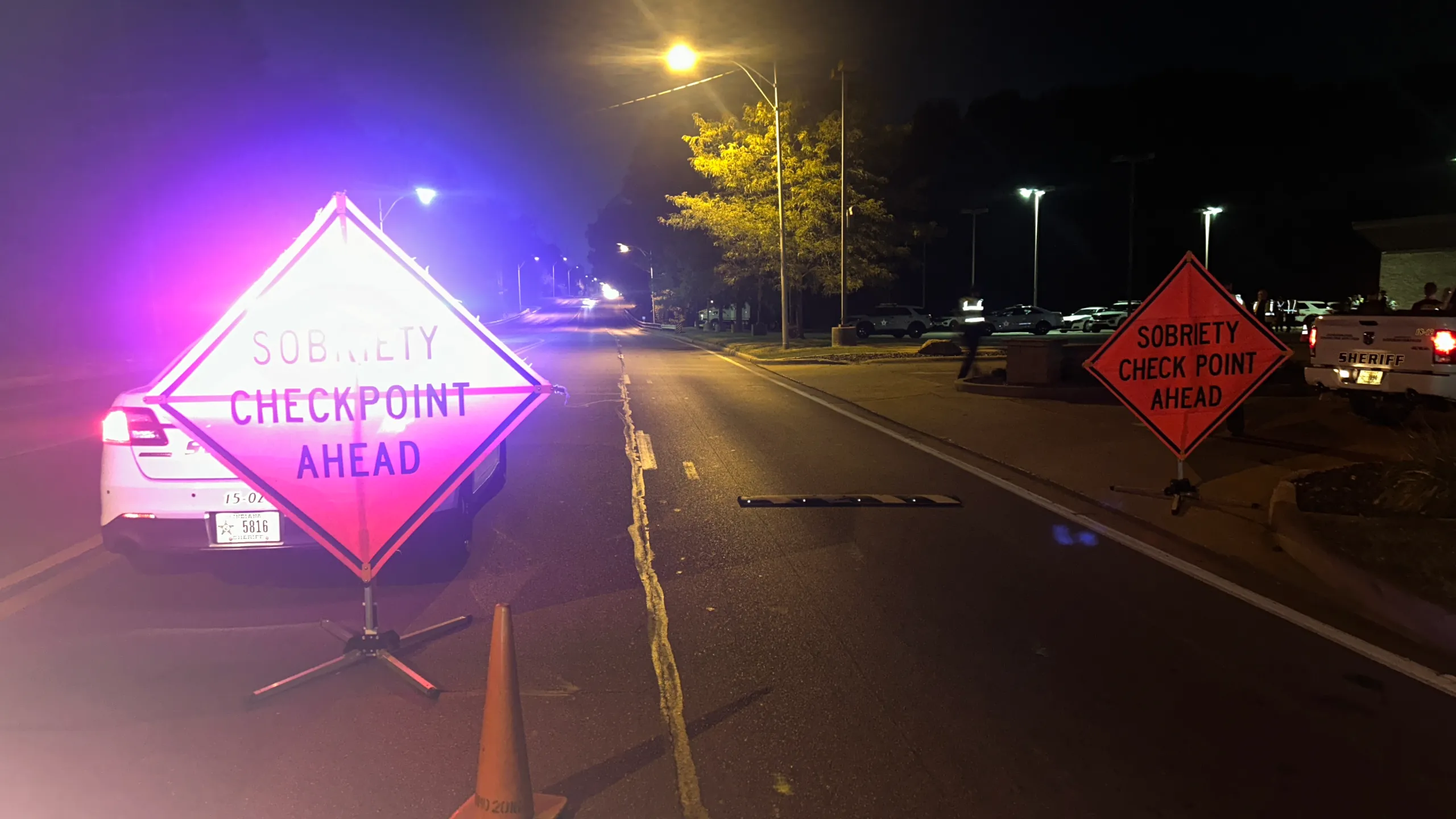A real DUI checkpoint setup with reflective traffic cones and a temporary road sign warning of a sobriety checkpoint ahead on a suburban roadway at night, news photography style