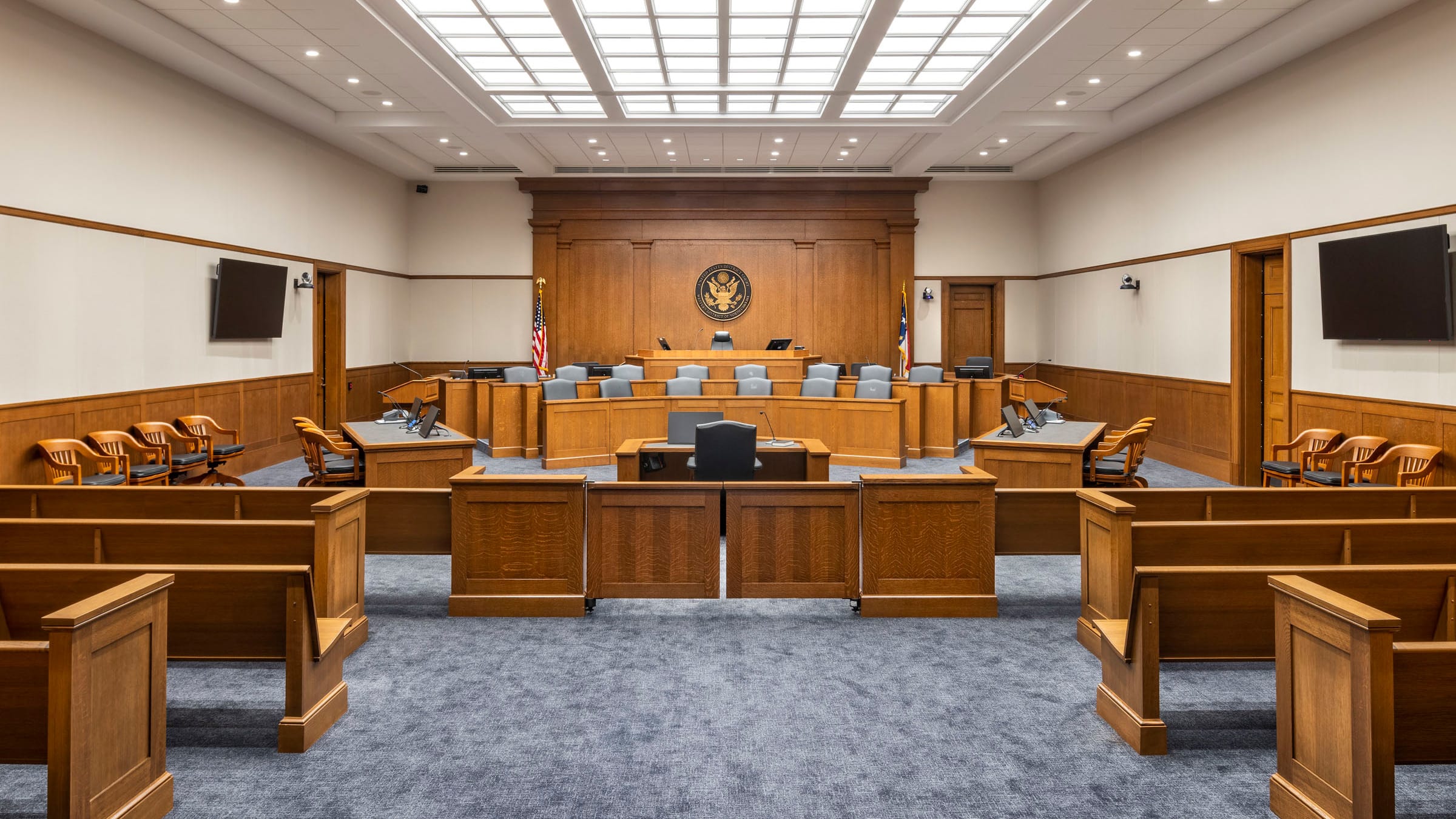 A real federal district courtroom interior photographed from the gallery, with the judge's bench, counsel tables, and the American flag visible, documentary news style