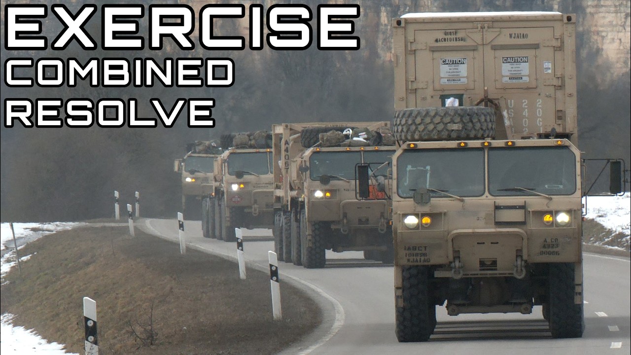 A real photo of a United States military vehicle convoy moving along a dusty road during a training exercise with service members visible, news photography style