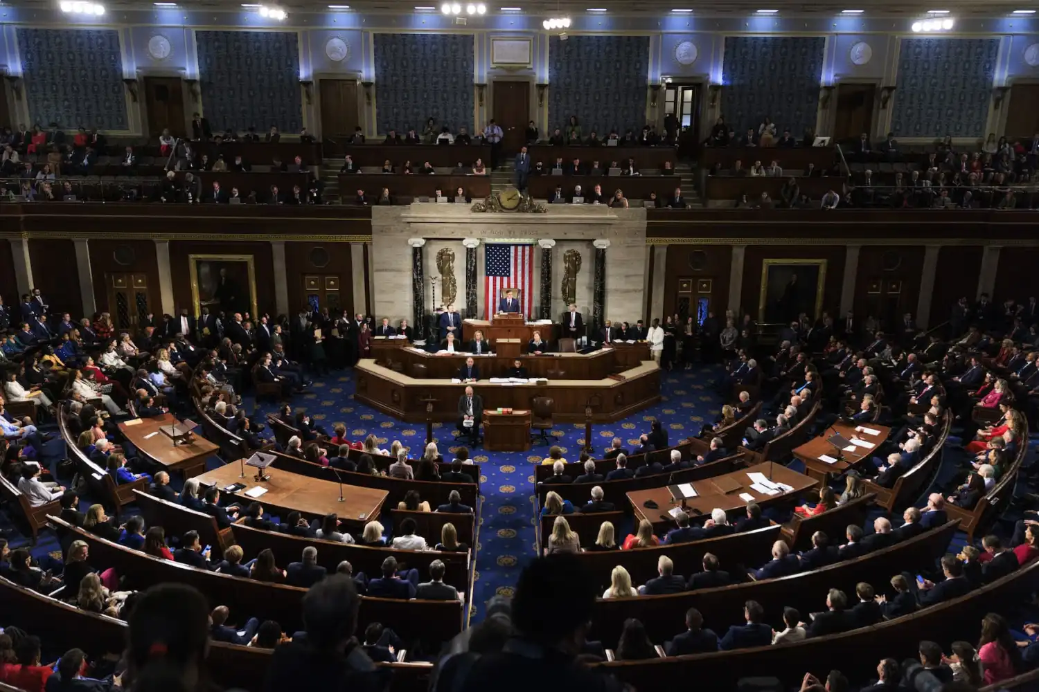 A real photograph inside the United States House of Representatives chamber during a legislative session with members seated and the dais visible, news photography style
