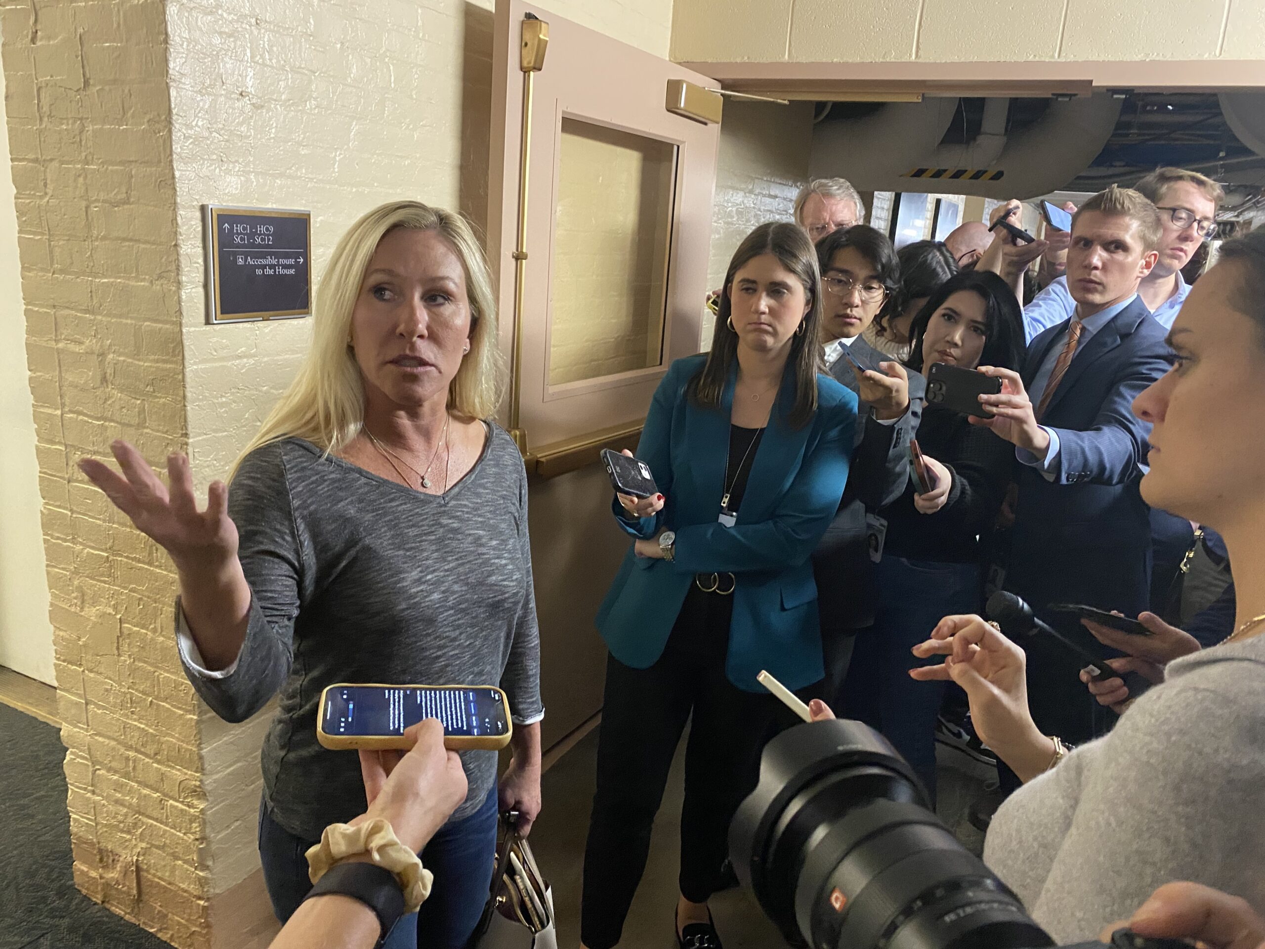 A real photograph of House leaders speaking to reporters in the United States Capitol hallway while microphones are held up, news photography style