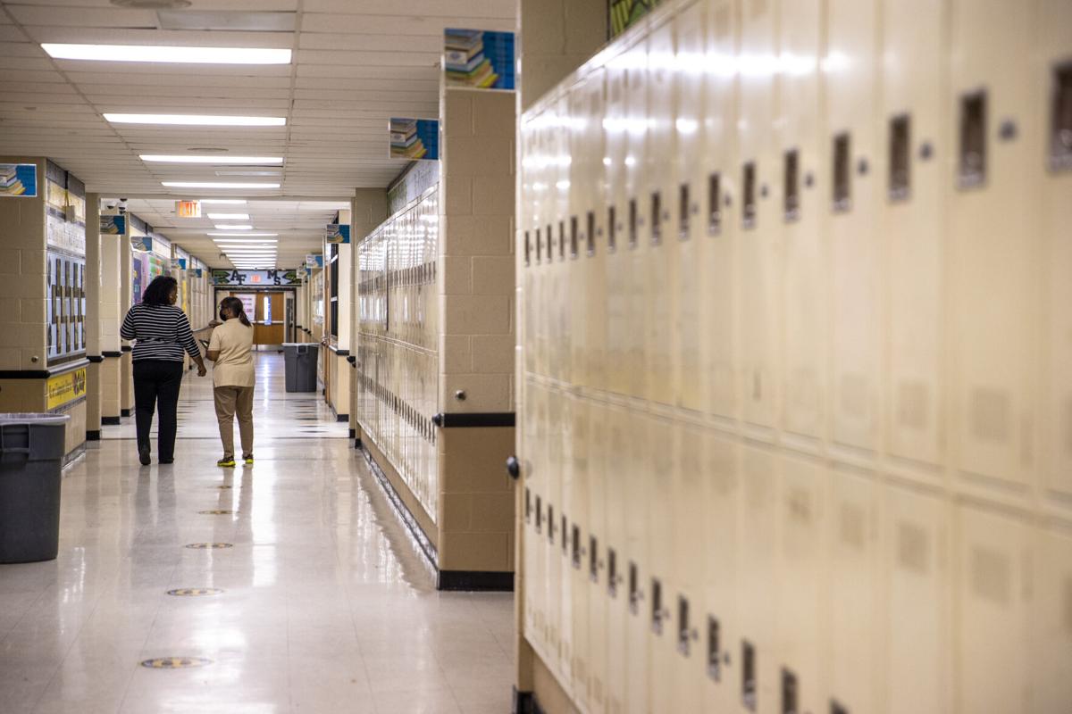 A real photograph of a school administrator speaking calmly with a student in a hallway, both standing near classroom doors, candid documentary style