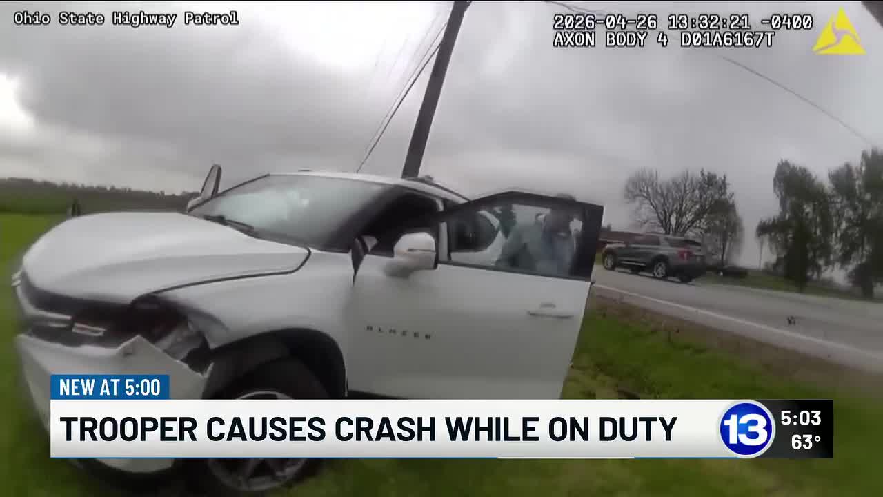 A real photograph of an officer documenting a crash scene on a highway shoulder with vehicles stopped nearby and traffic cones set out, news photography style