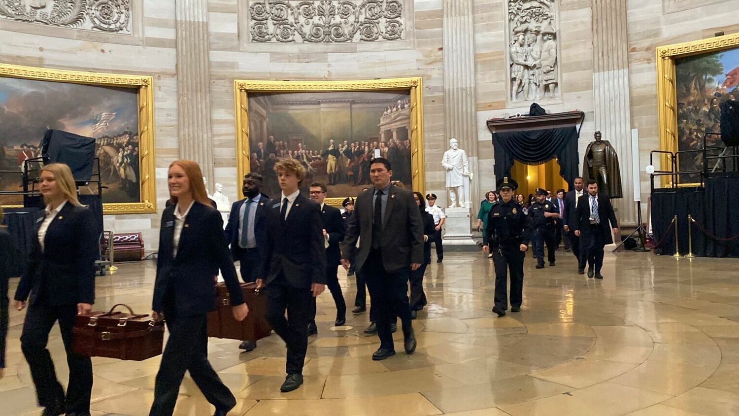 A real photograph of senators and staff walking in a hallway near the U.S. Senate chamber inside the United States Capitol, candid news photography style