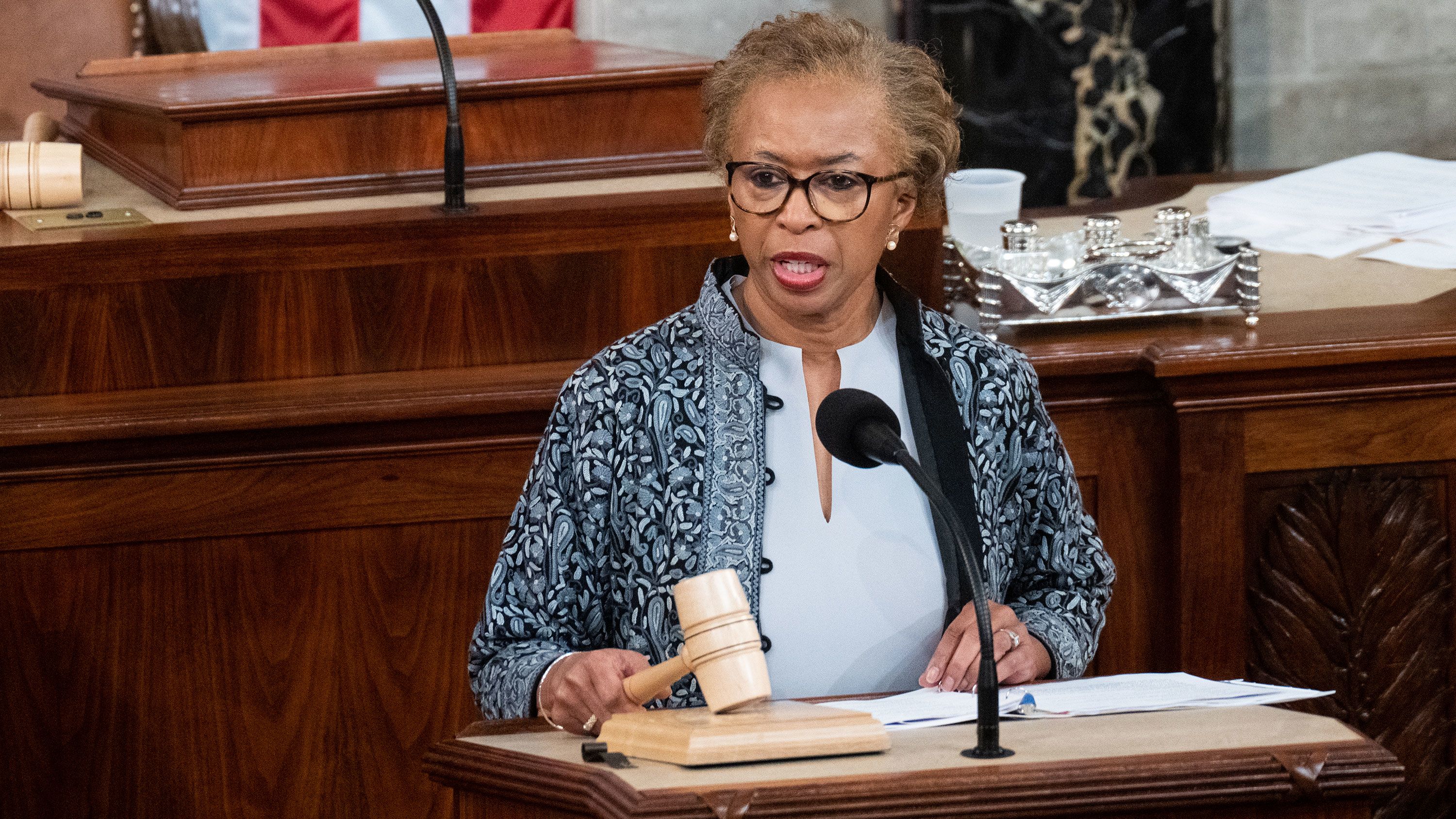 A real photograph of the Clerk at the House rostrum reading names during a roll call vote while members watch from the floor, news photography style