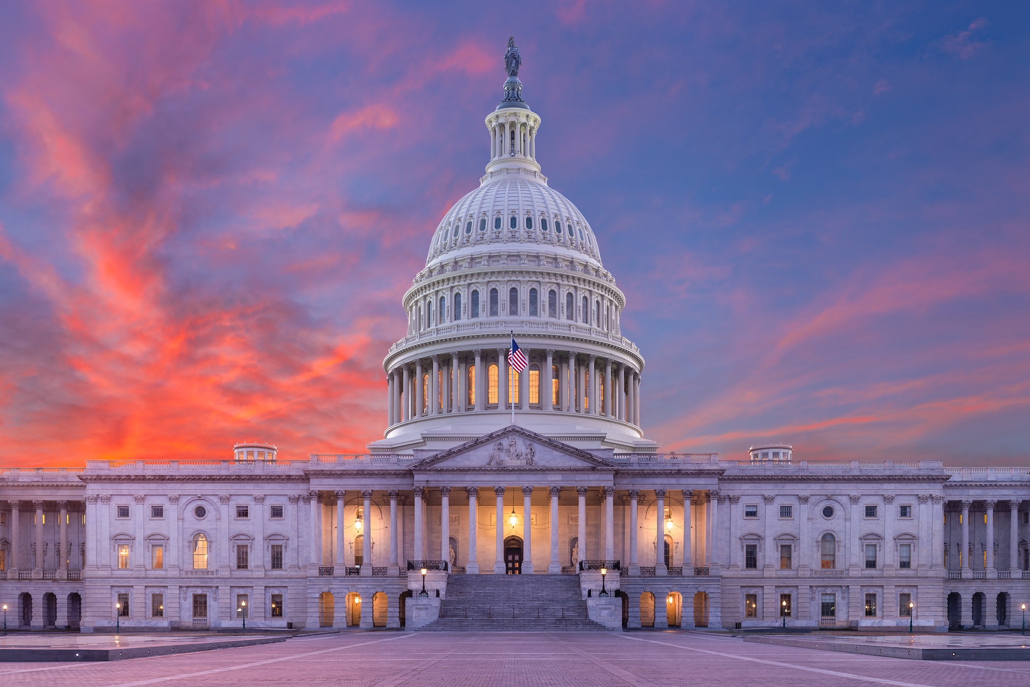 A real photograph of the United States Capitol building at dusk with warm interior lights and a clear view of the dome, news photography style
