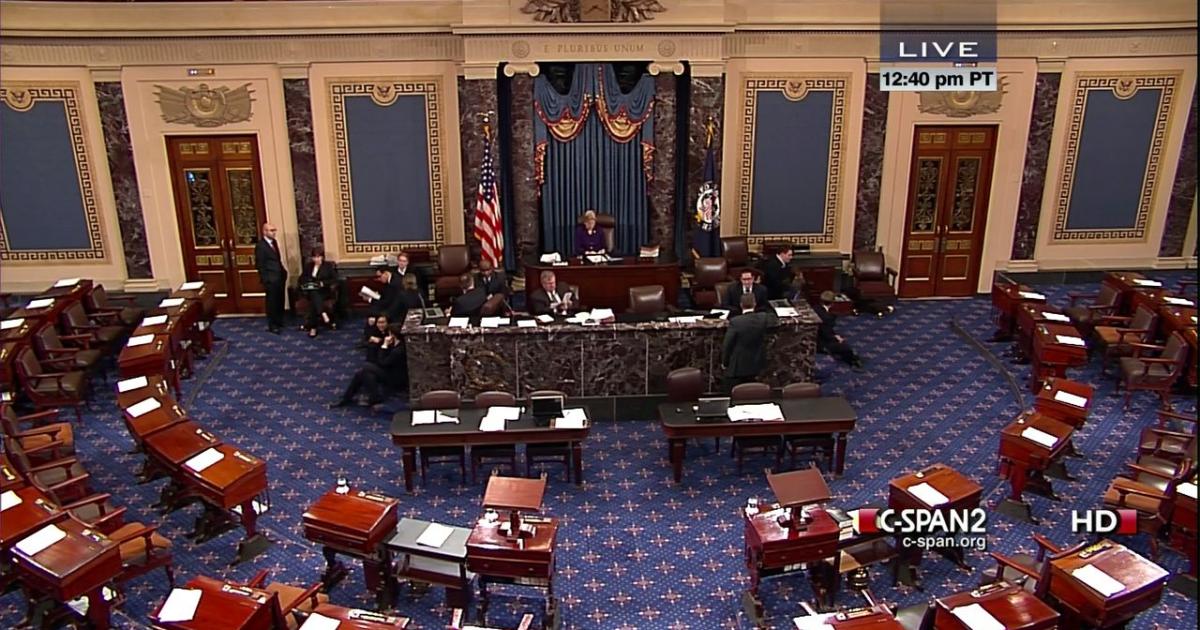 A real photograph of the United States Senate chamber during a quiet quorum call, with a few senators and staff visible and the presiding officer at the dais