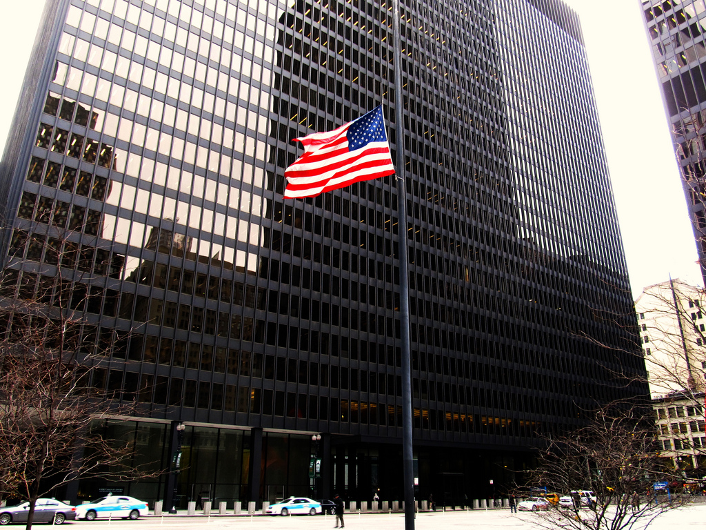A real-world photograph of a federal courthouse interior showing the U.S. District Court clerk’s office sign and people walking through the hallway