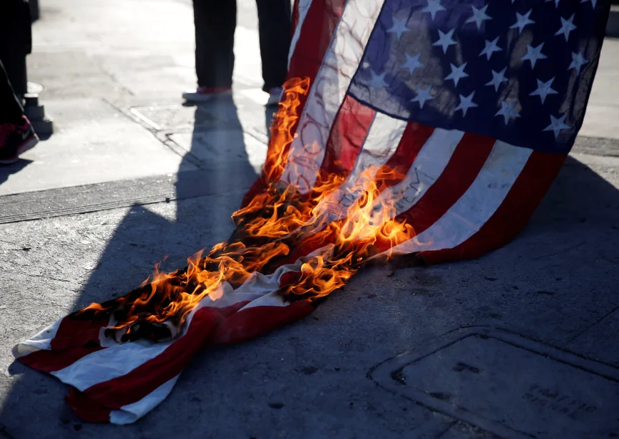 A real-world photograph of flag burning during a public protest associated with the Texas v. Johnson era, illustrating the Supreme Court’s symbolic speech doctrine