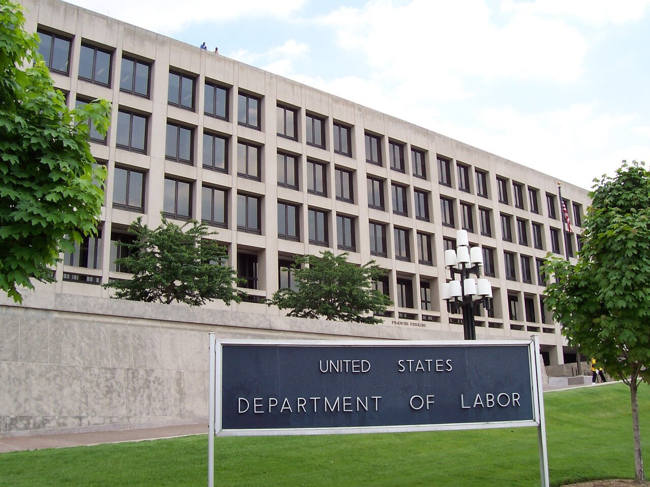 A real-world photograph of the United States Department of Labor building exterior in Washington, DC on an overcast day