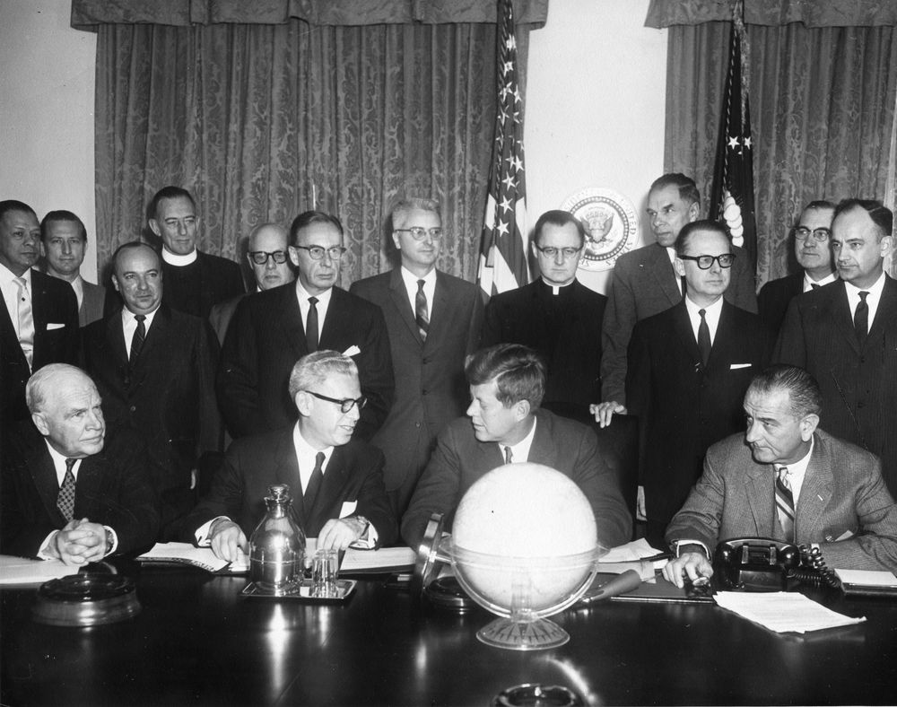 A realistic mid-1960s office scene of staff working at desks in an Equal Employment Opportunity Commission office in Washington, D.C., documentary news photography style