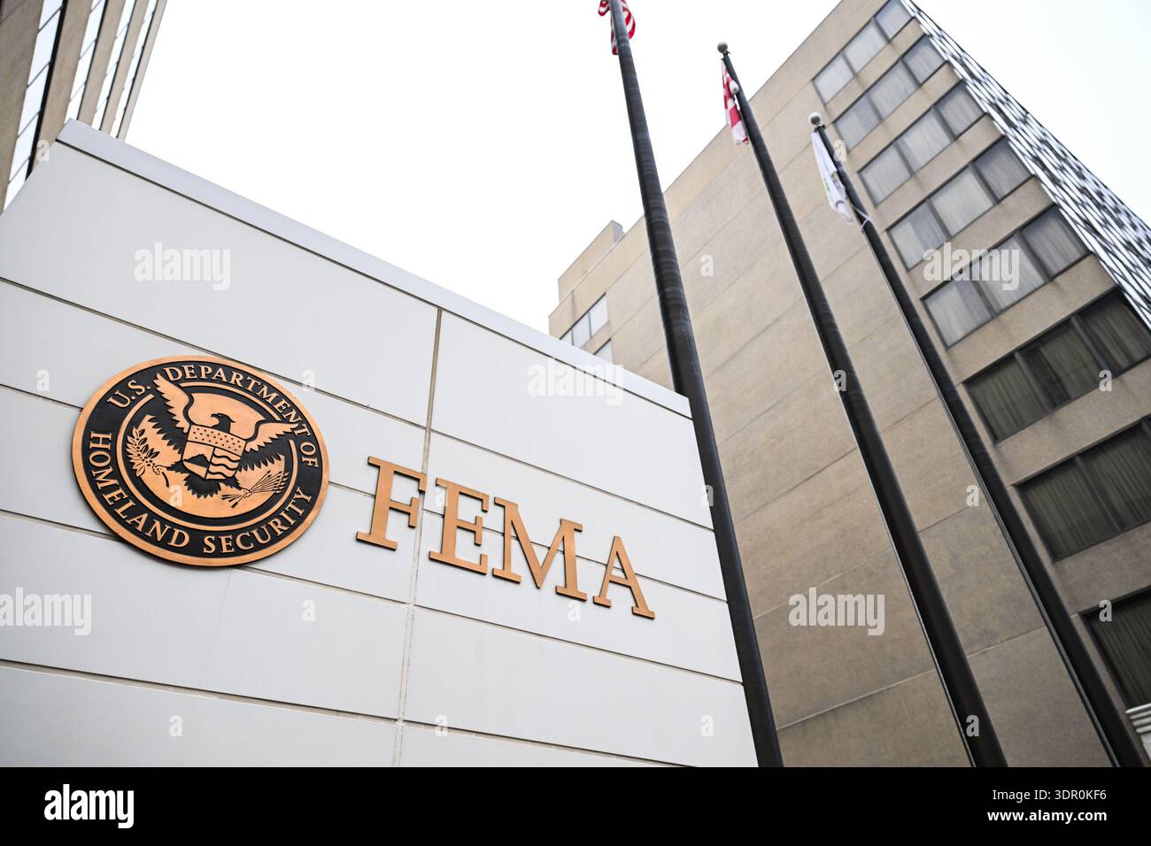 A realistic street-level photograph of a modern federal agency headquarters building in Washington, DC, with pedestrians on the sidewalk and no visible signage readable
