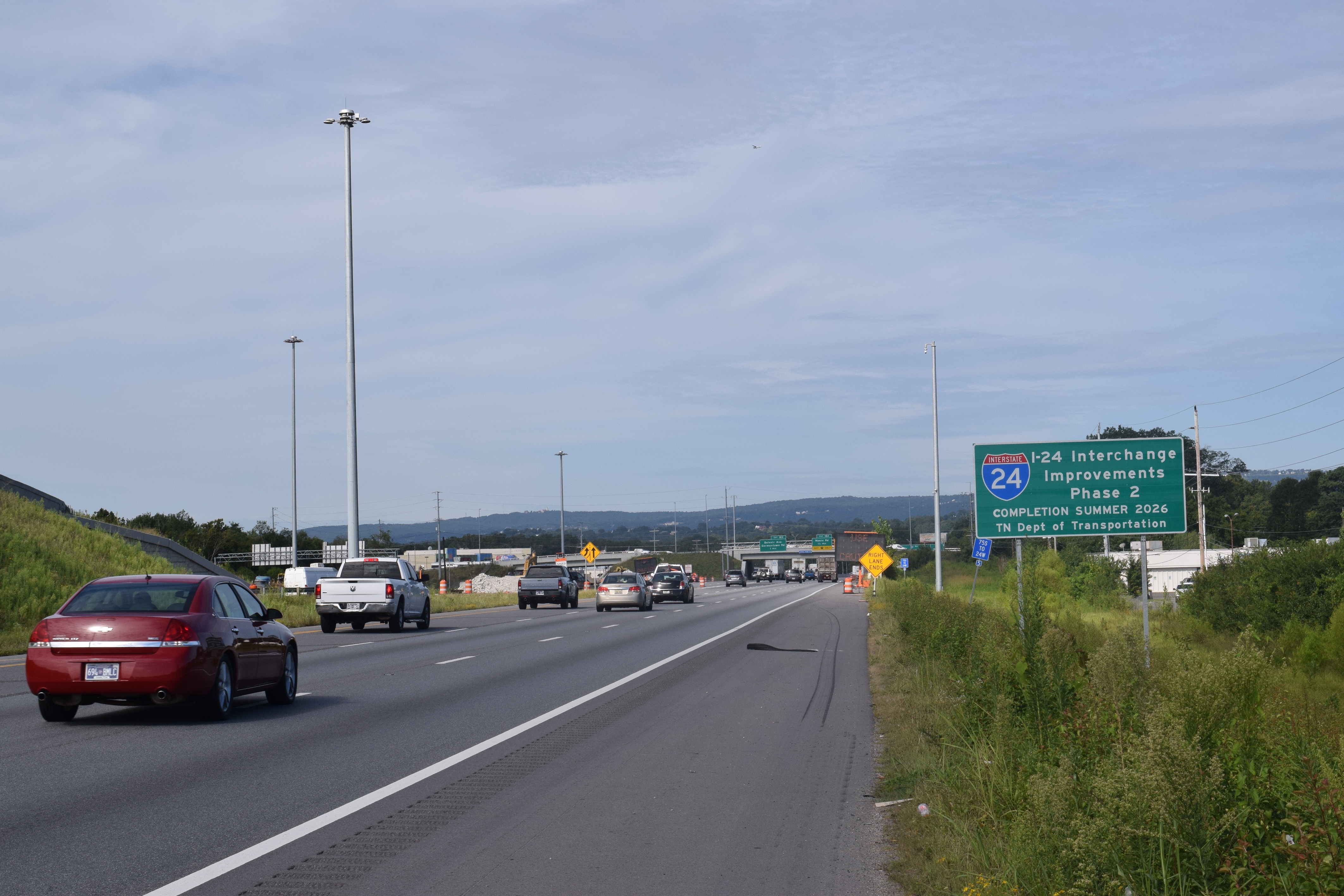 A roadside state border sign on an interstate highway with cars passing by in the background, photographed as a real travel scene