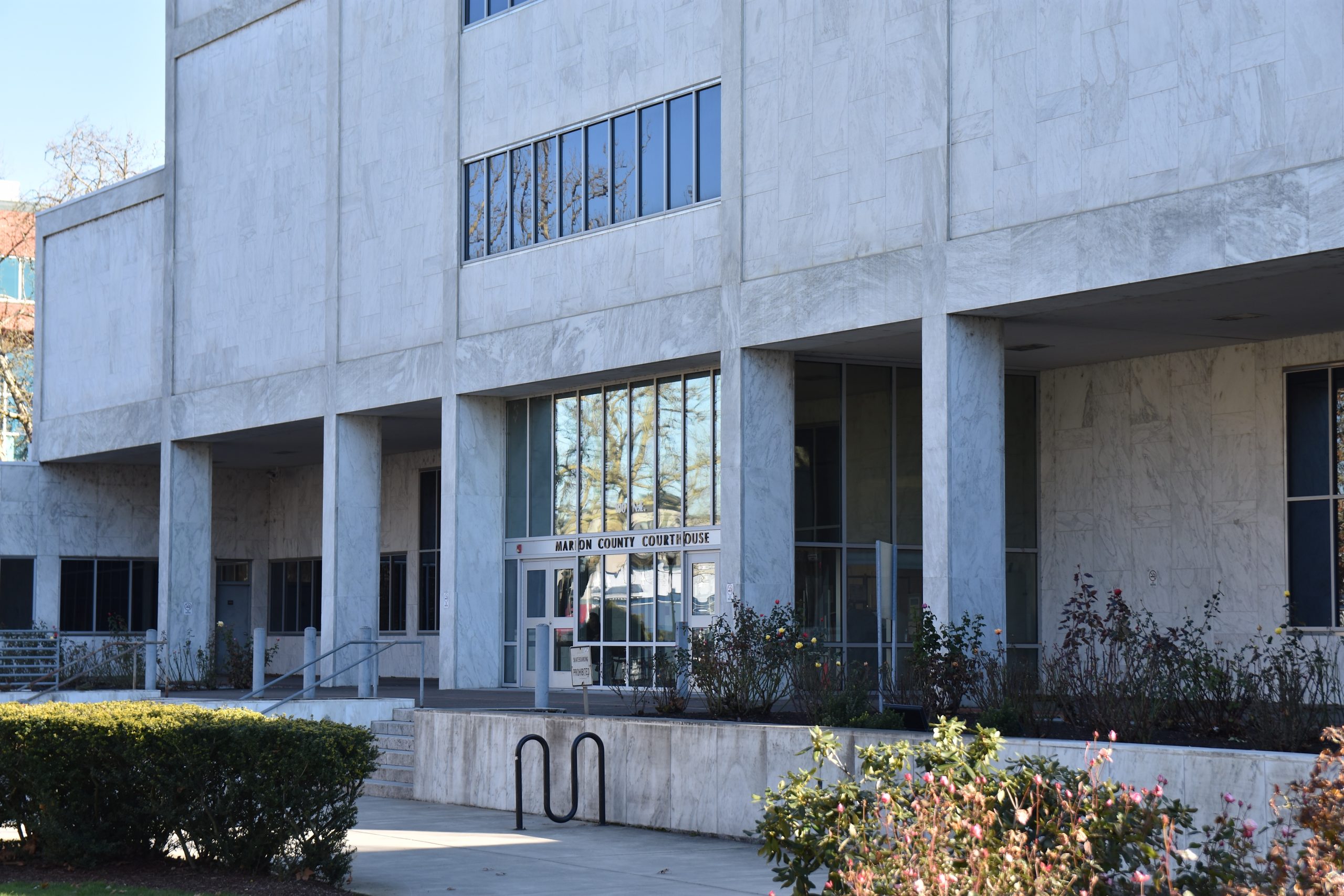 A sheriff's deputy walking up the steps of a county courthouse with a suited attorney nearby, midday sunlight, news photography style