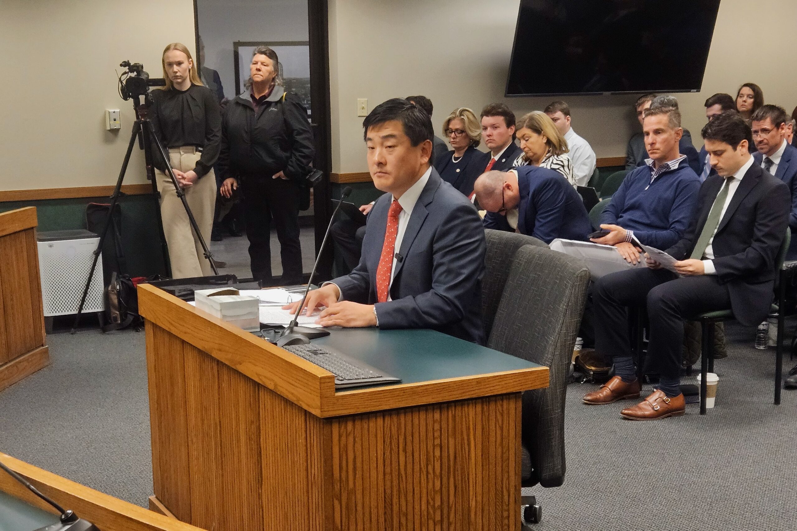 A state government tax office service counter with a clerk assisting a citizen across a glass partition, documentary news photography style