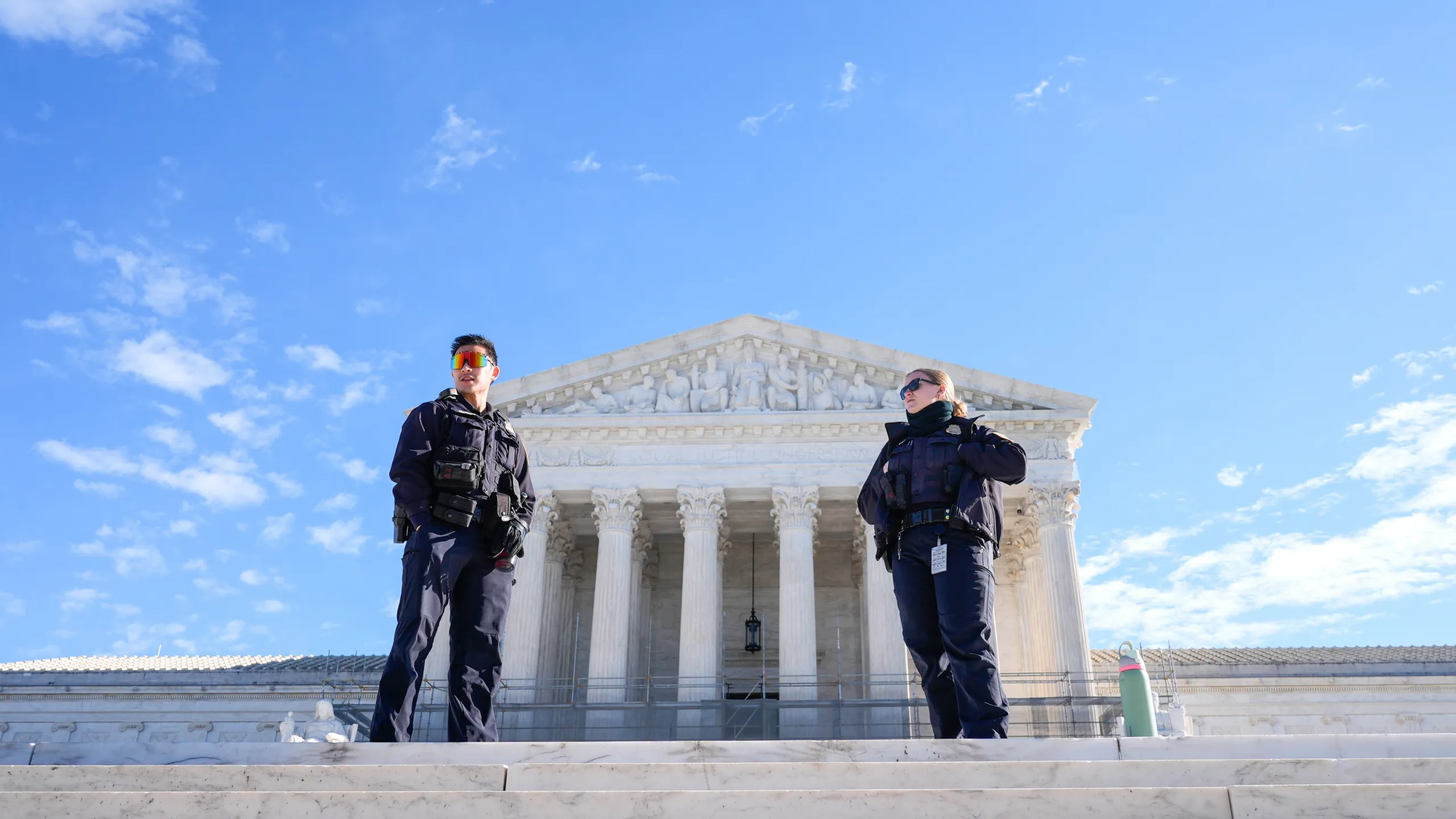 A uniformed Supreme Court police officer standing outside the Supreme Court building entrance in Washington, DC, with pedestrians in the background, news photography style