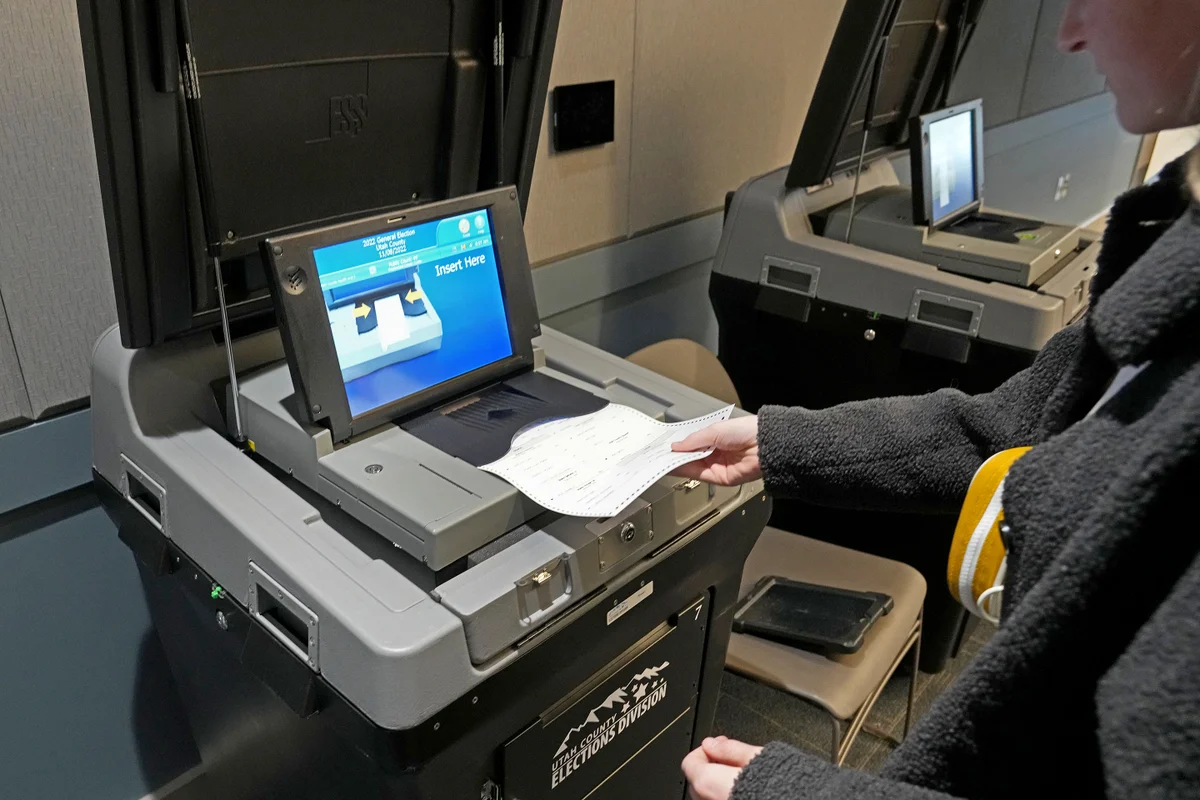 A voter inserting a completed ballot into a secure ballot scanner on general election day inside a polling place, real editorial news photo