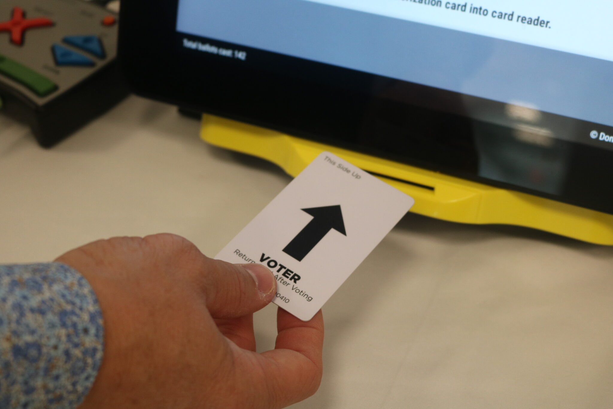 A voter’s hand inserting a paper ballot into an election scanner at a polling place in the United States during a midterm election, news photography style
