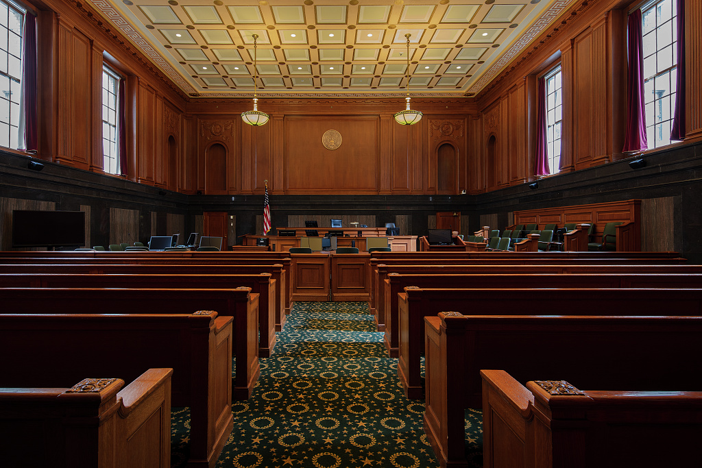 A wide-angle photograph of a United States Court of Appeals courtroom with empty counsel tables facing the judge's bench, warm indoor lighting, formal government interior