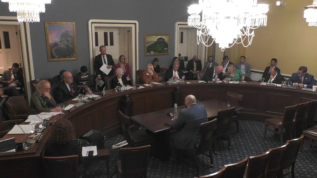 A wide-angle photograph of the U.S. House Rules Committee hearing room with members seated at the dais and staff at tables, documentary news photography style