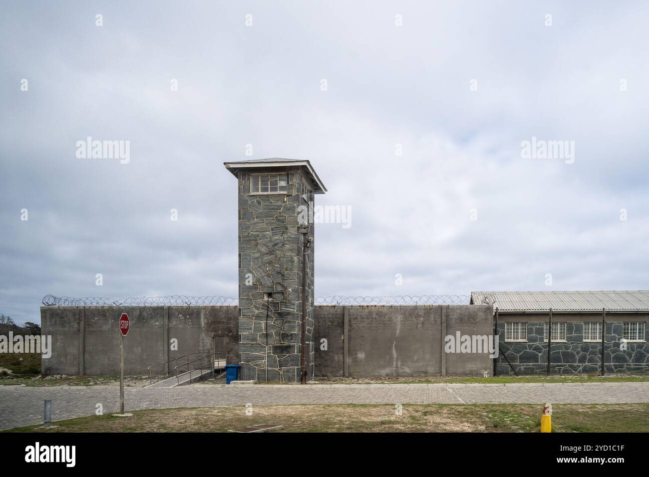 A wide exterior view of a detention facility with perimeter fencing and a guard tower in the distance, news photography style