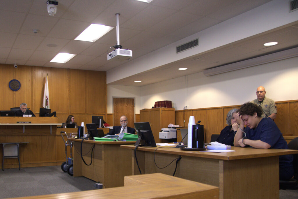 A wide shot of a courtroom during an arraignment hearing with the judge on the bench and attorneys standing at counsel tables, news photography style