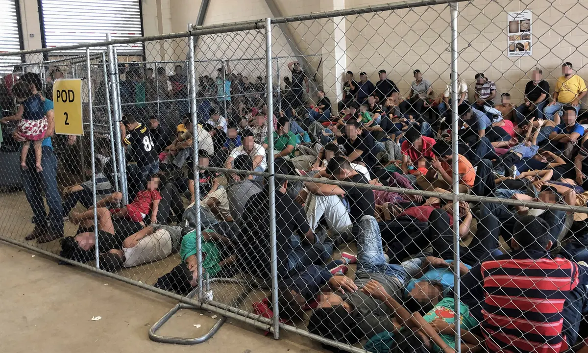 A wide shot of the exterior of a detention facility in Texas with a chain-link perimeter fence and law enforcement vehicles staged nearby, news photography style