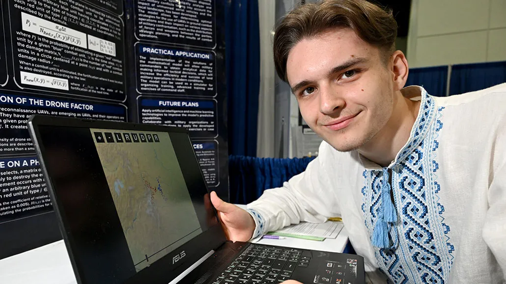 A young man seated at a kitchen table using a laptop to complete an online government form, documentary style photography