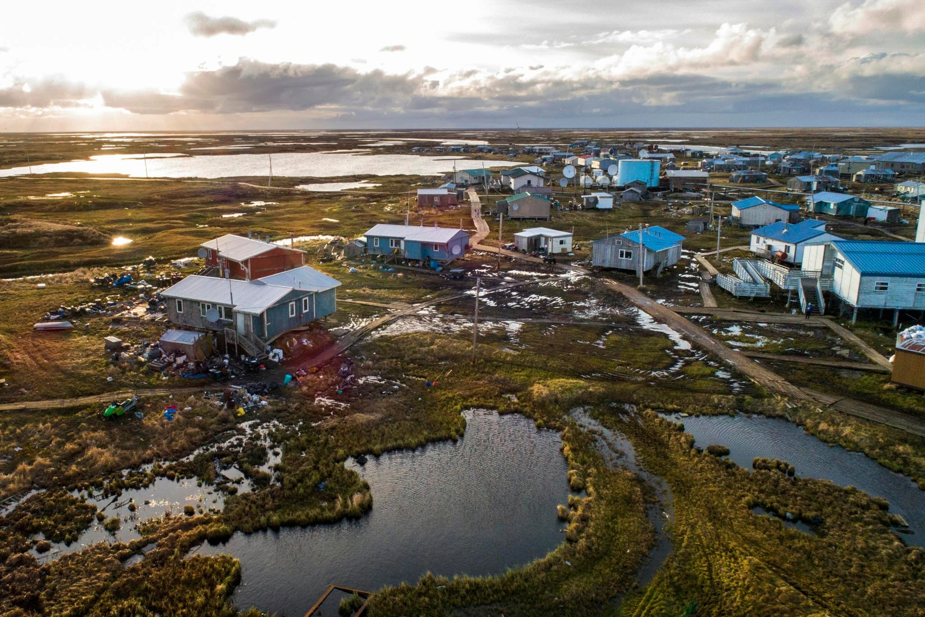 Aerial photograph of Platinum, Alaska, a small coastal community on the Bering Sea with clustered buildings and surrounding tundra, news photography style