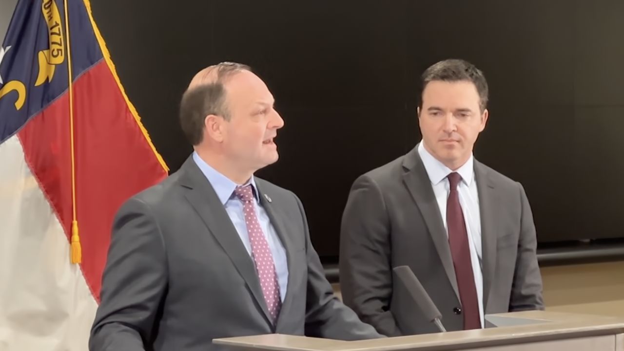 Alan Wilson, South Carolina attorney general, speaking at a press conference with microphones and state flags behind him, news photography style
