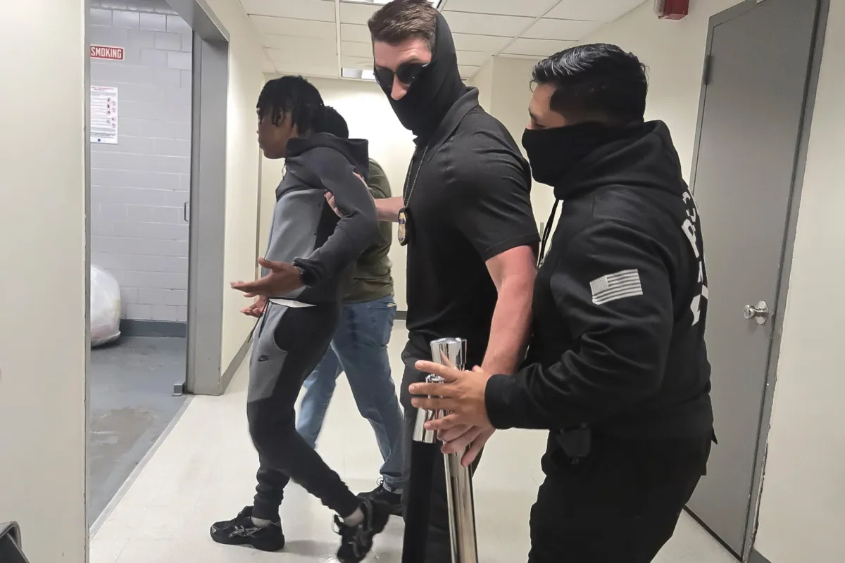 An ICE detainee in handcuffs standing beside defense counsel in a federal courtroom during a May 2026 hearing, news photography style