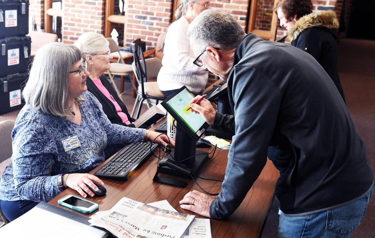 An election worker verifying a voter’s registration on a laptop at a check-in table during a November election, candid news photography style
