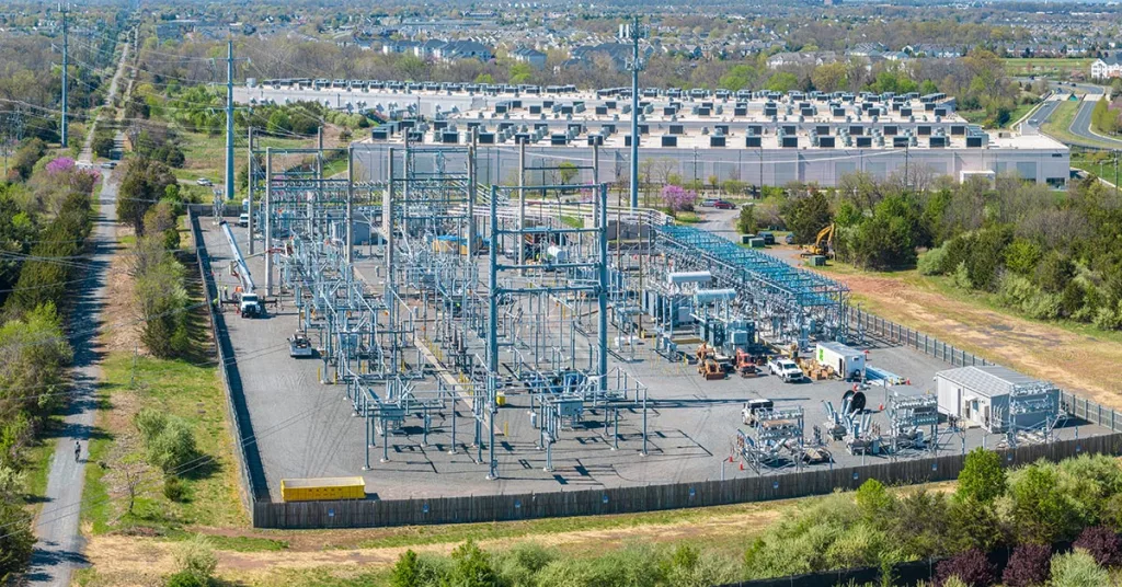 An exterior view of a data center electrical substation with transformers and high-voltage equipment behind a security fence