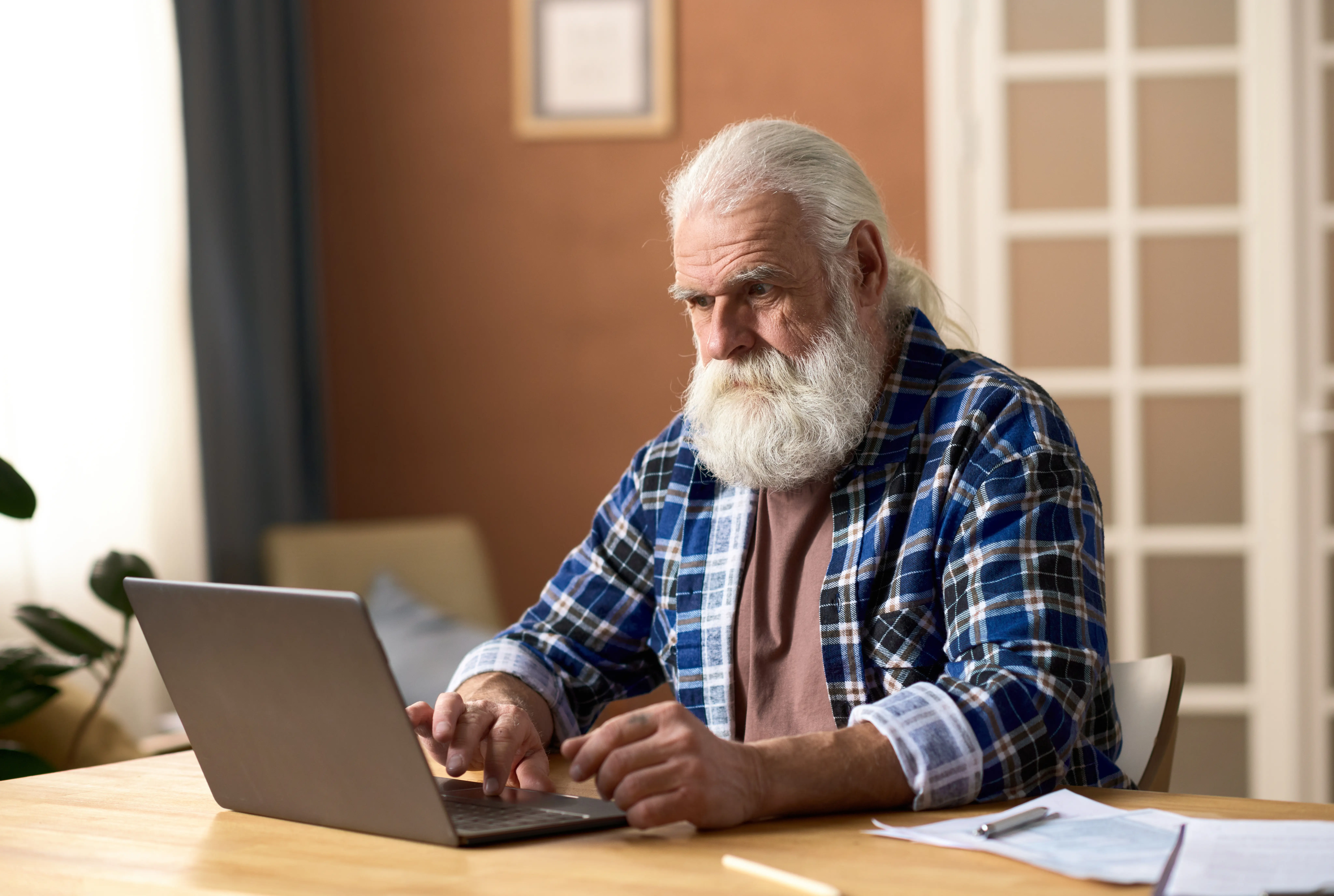 An older adult seated at a desk using a laptop to check an online government account, soft indoor lighting, realistic documentary photograph
