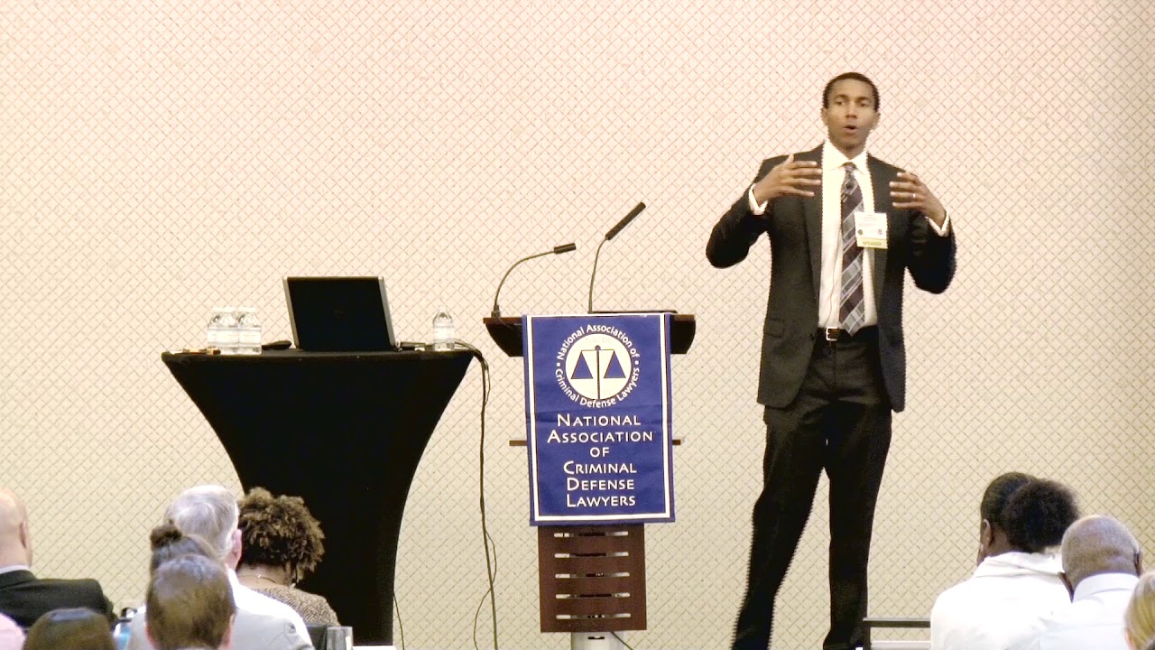 Brandon Buskey speaking at a podium indoors during a legal policy event, candid news photography style