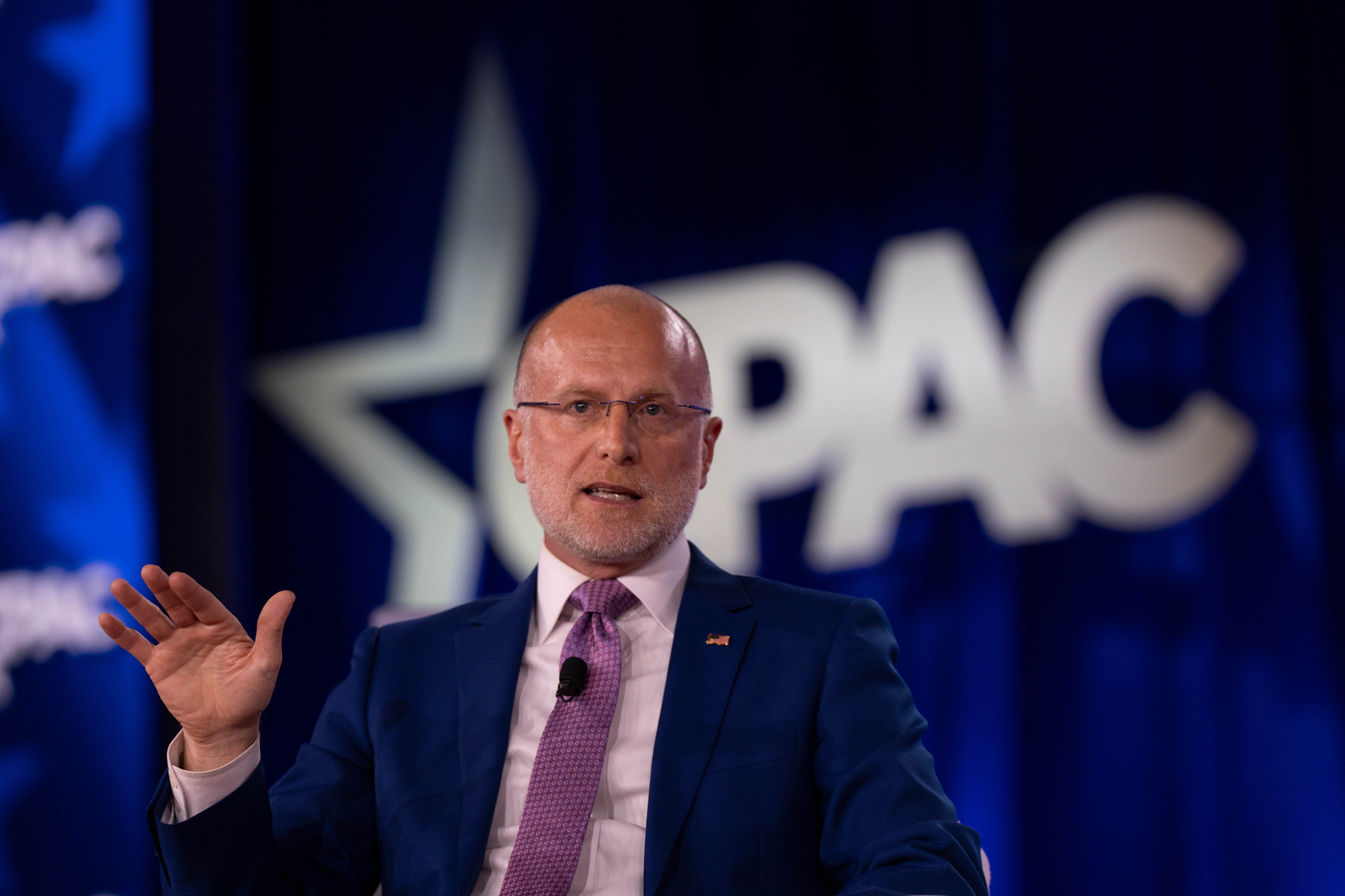 Brendan Carr seated at a dais during a Federal Communications Commission meeting, microphones and nameplates visible, news photography style