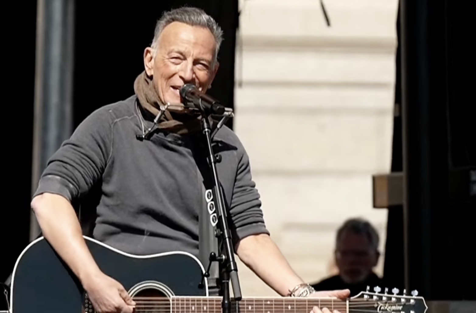 Bruce Springsteen performing on an outdoor stage in St. Paul, Minnesota, with a guitar and microphone as a large crowd watches, news photography style
